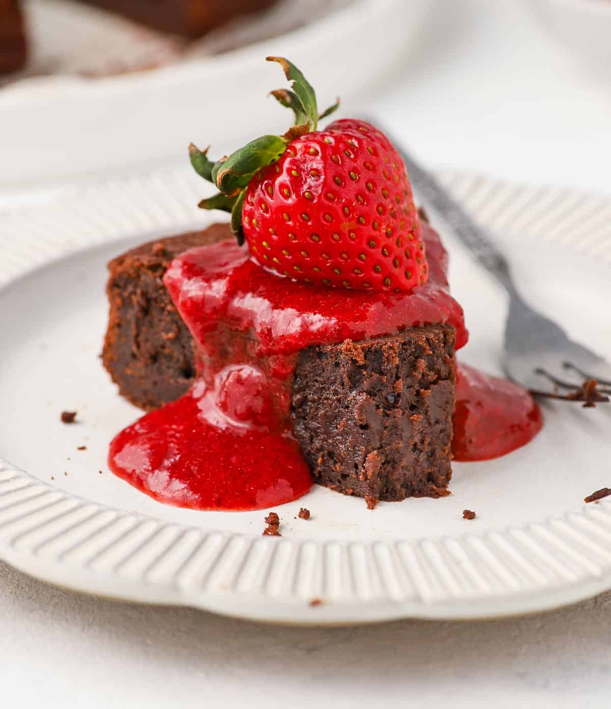 Sauce poured over a slice of chocolate cake and topped with a strawberry.