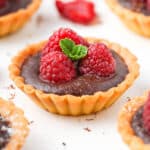 Close up on a chocolate raspberry tartlet on a white surface.