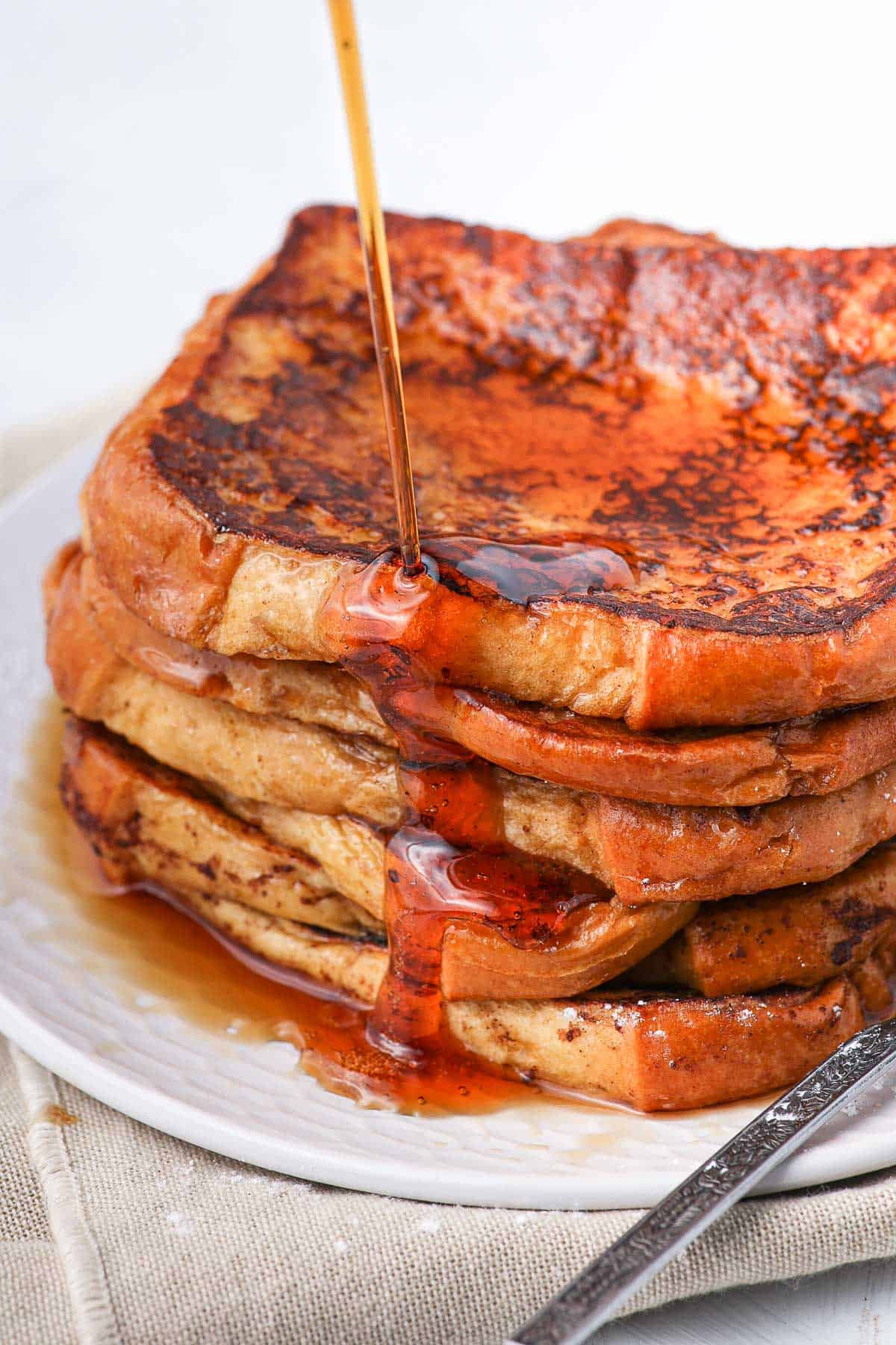 Pouring maple syrup over a stack of french toast.