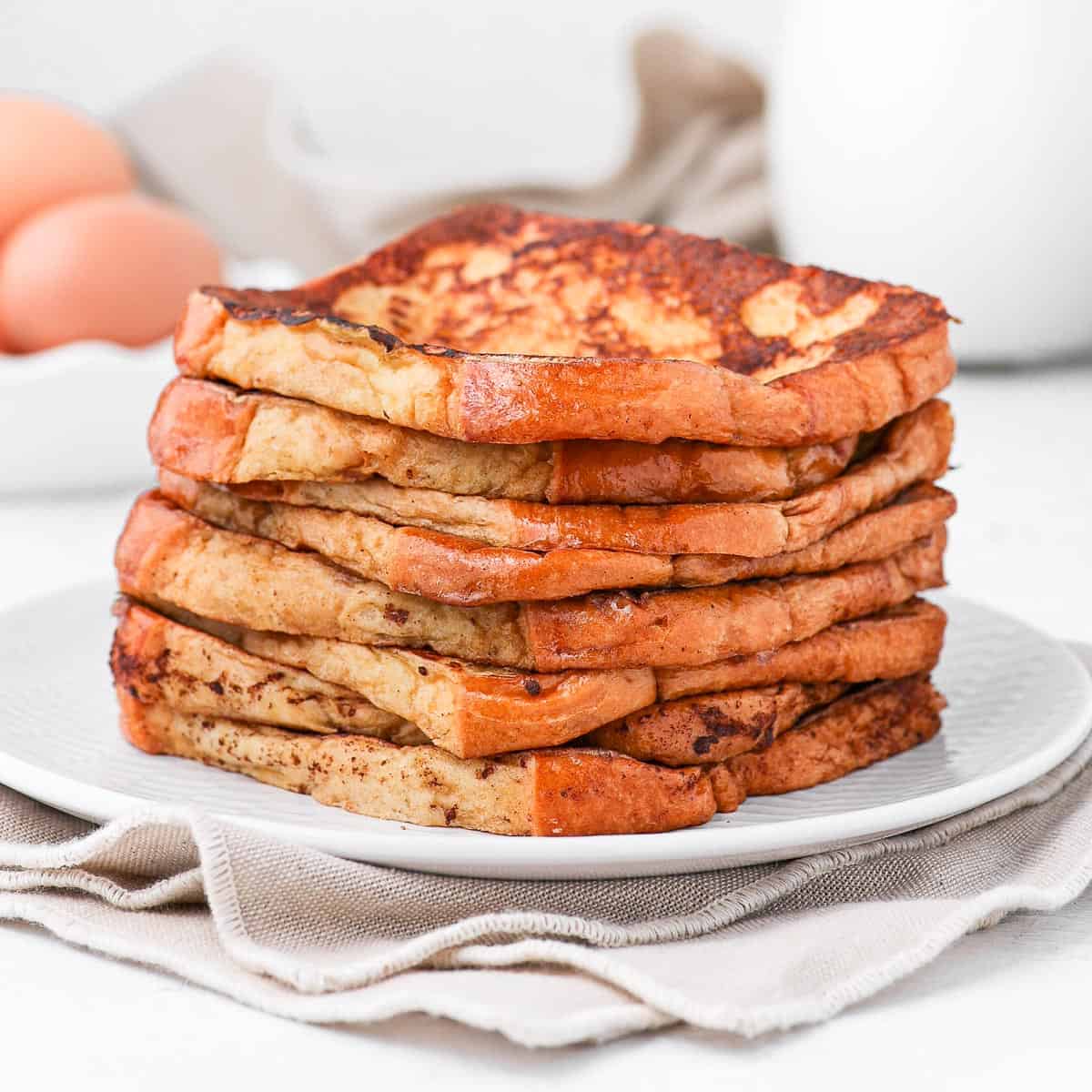 Brioche french toasts stacked on a white plate over a beige napkin.