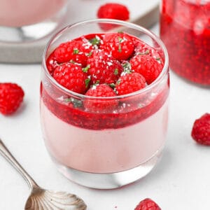 Close up on a raspberry panna cotta cup with fresh raspberries and some mint.