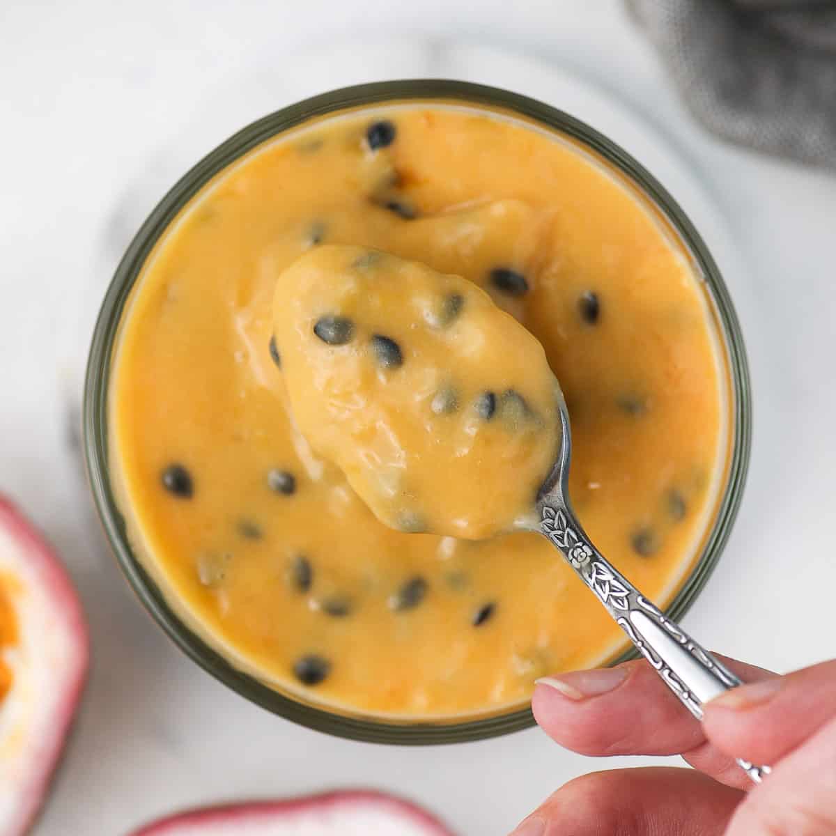 Picking up some passion fruit curd from a jar with a spoon.