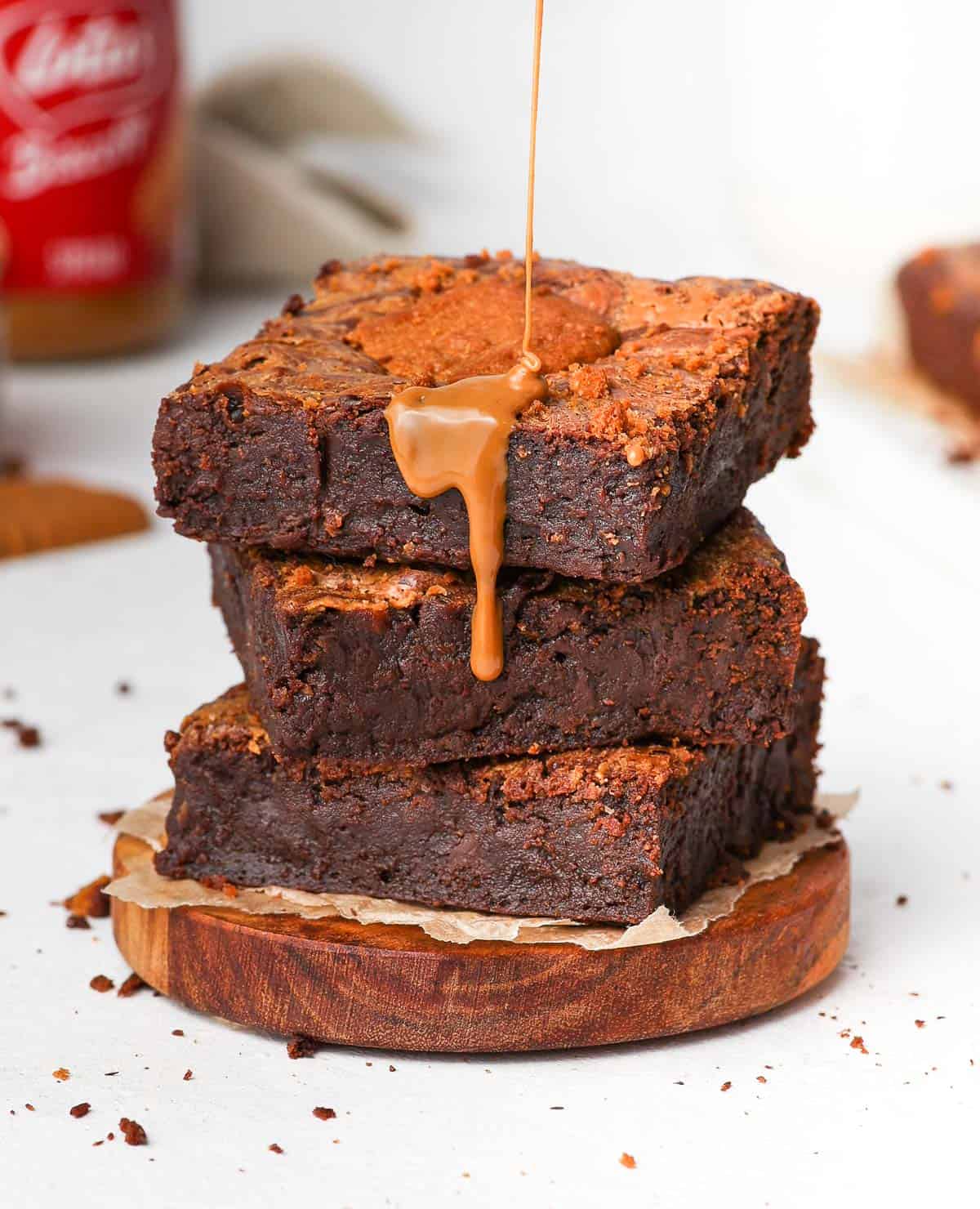 Pouring biscoff spread over a stack of three brownie slices.