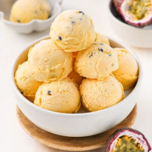 Scoops of ice cream stacked in a white bowl surrounded by fresh passion fruit.