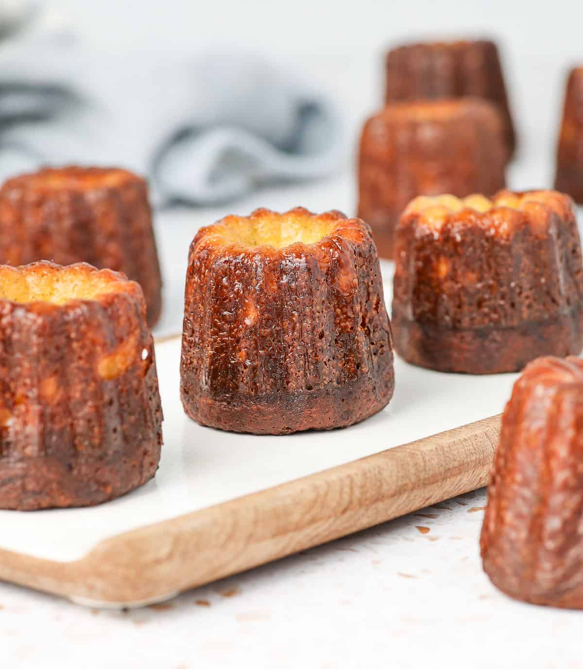 Caneles on aserving board with a light white napkin in the background.