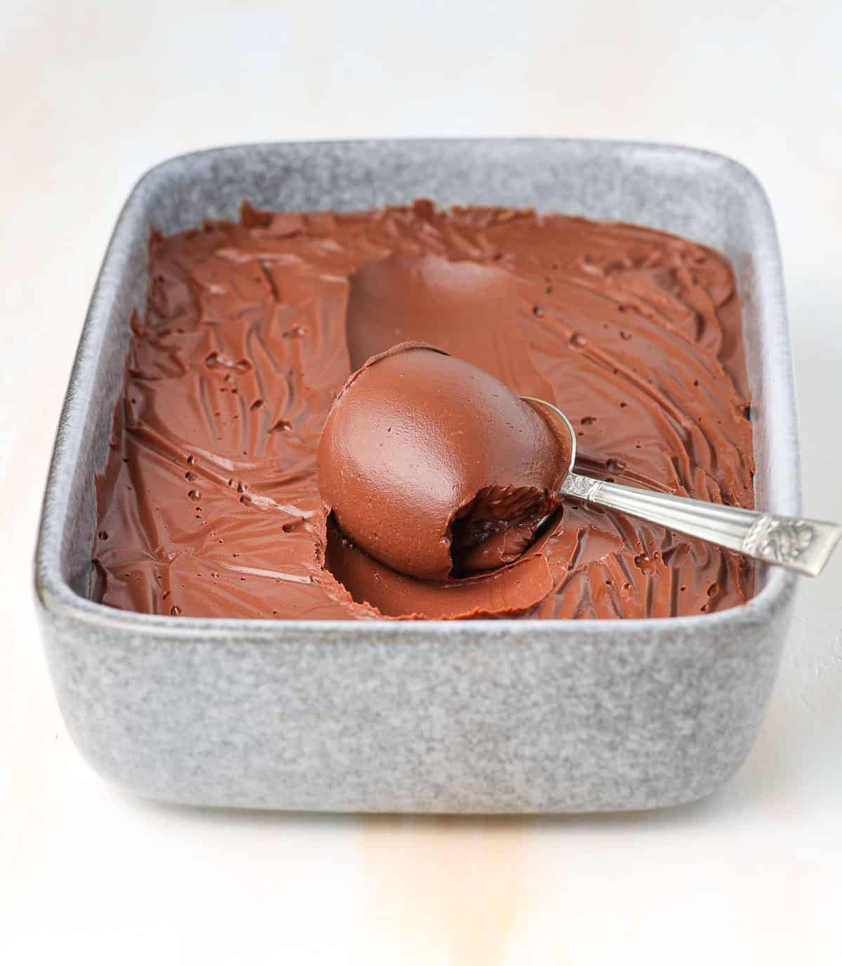 Cremeux in a grey baking dish with a scoop rolled on a spoon.