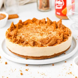 Biscoff Cheeecake topped with chunks of biscoff cookies on a white plate over a white surface,