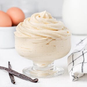 Cream piped in a glass cup surrounded by vanilla bean, eggs and milk.