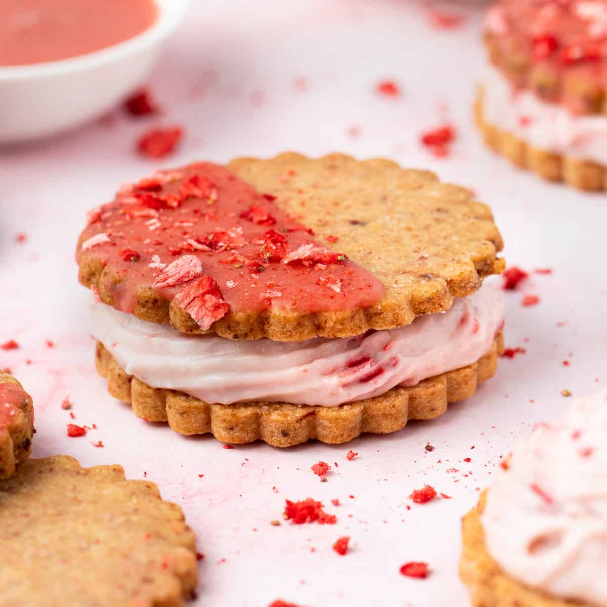 Close up on one cookie over a pink surface surrounded by freeze dried strawberry crumbs.