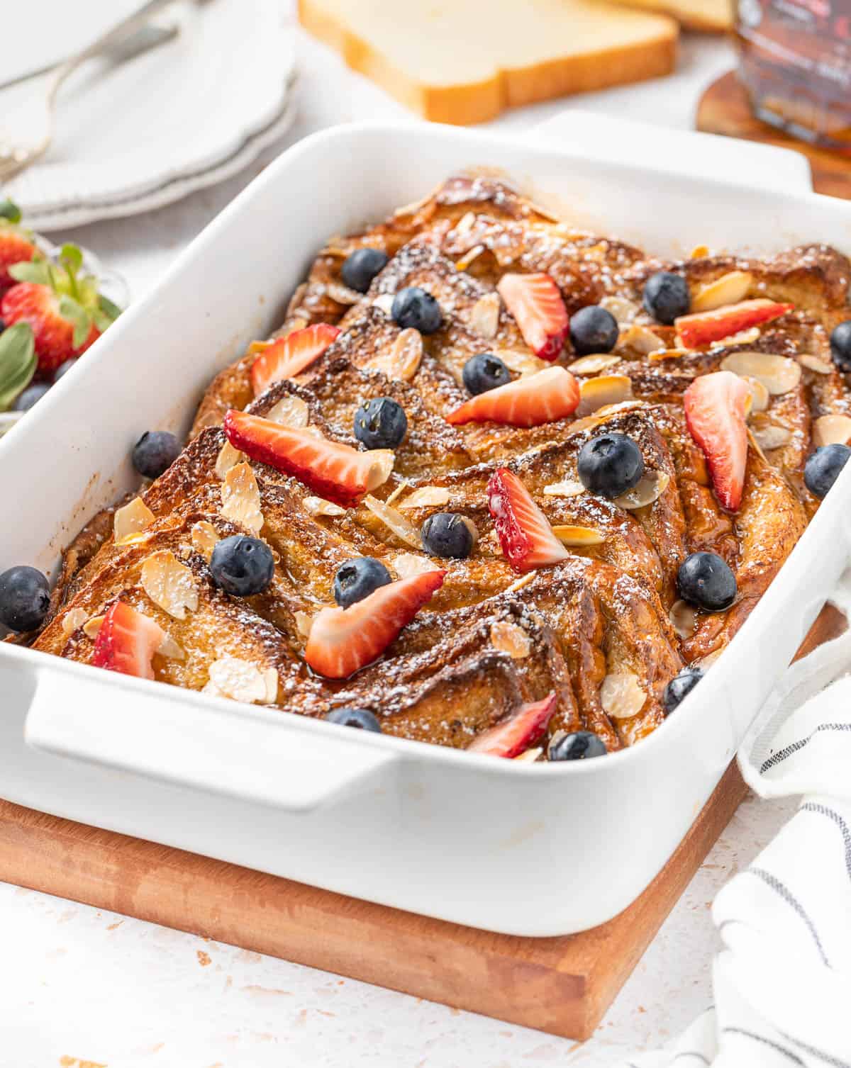 French toast bake in a white ceramic baking dish over a wooden cutting board.