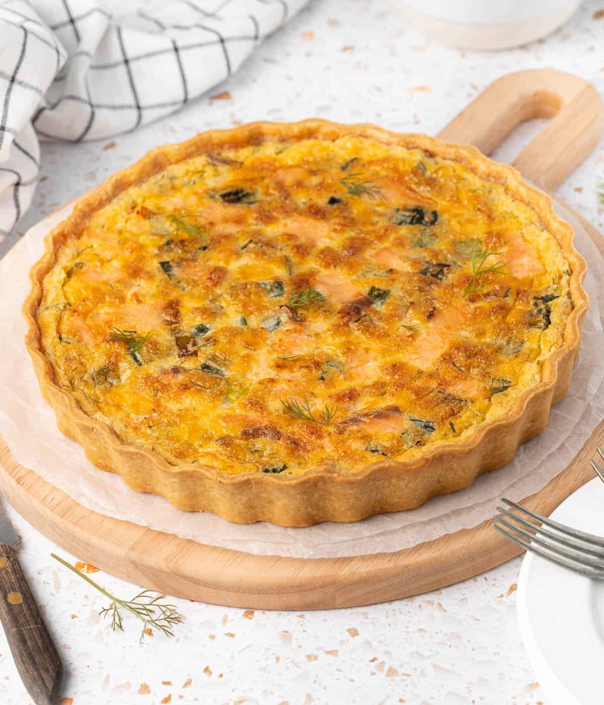Baked quiche on a round wooden serving board.