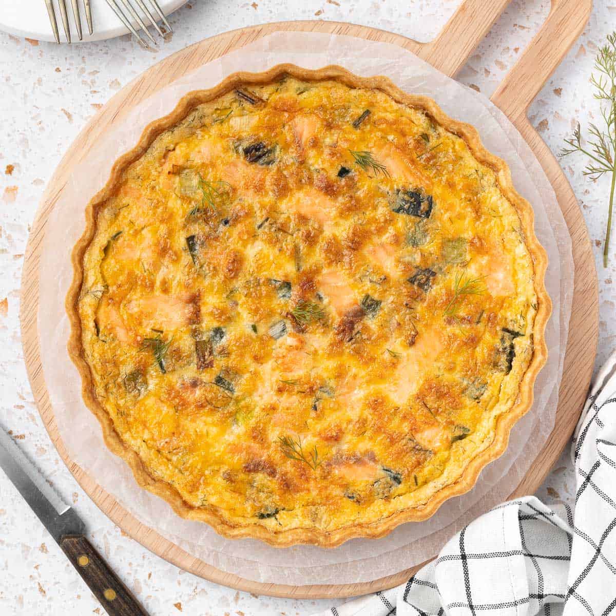 Salmon Quiche seen from above over a round wooden board and white baking paper sheets.