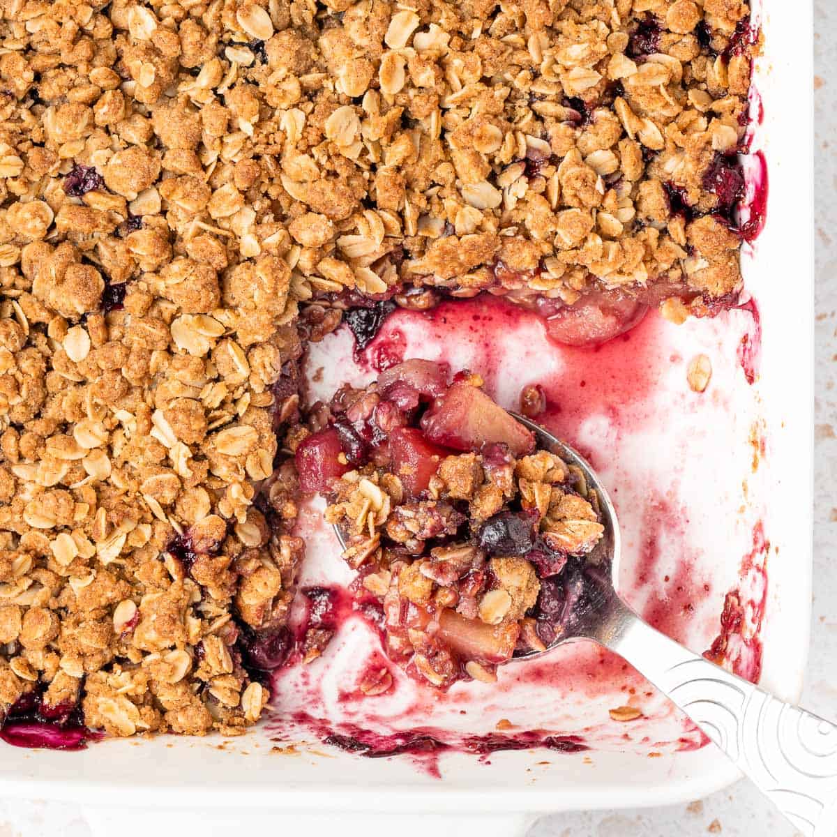 Close up on a large spoon filled with crumble inside the baking dish.