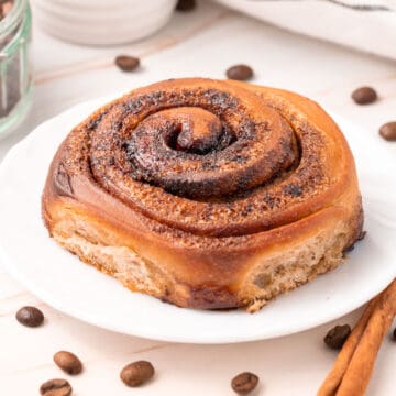 Close up on a roll over a small white plate surrounded by coffee beans