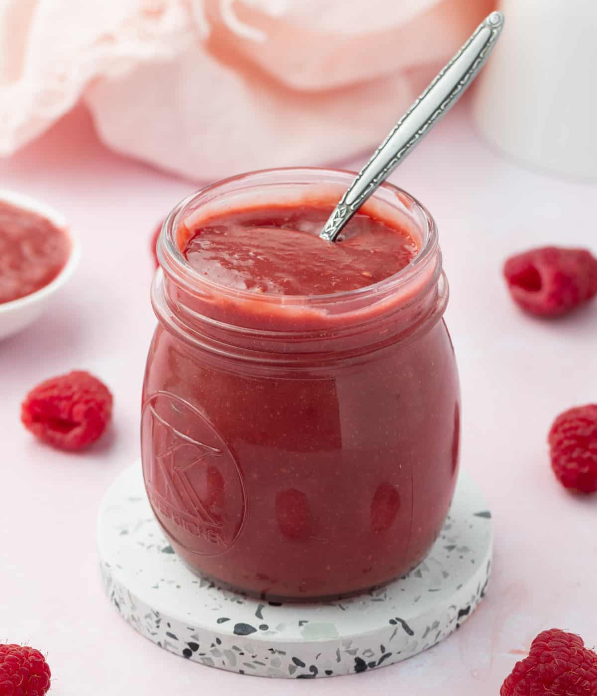 Curd inside a glass jar with a silver spoon on a pink background.