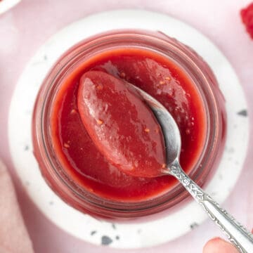 Picking up some raspberry curd from a jar with a spoon seen from above.