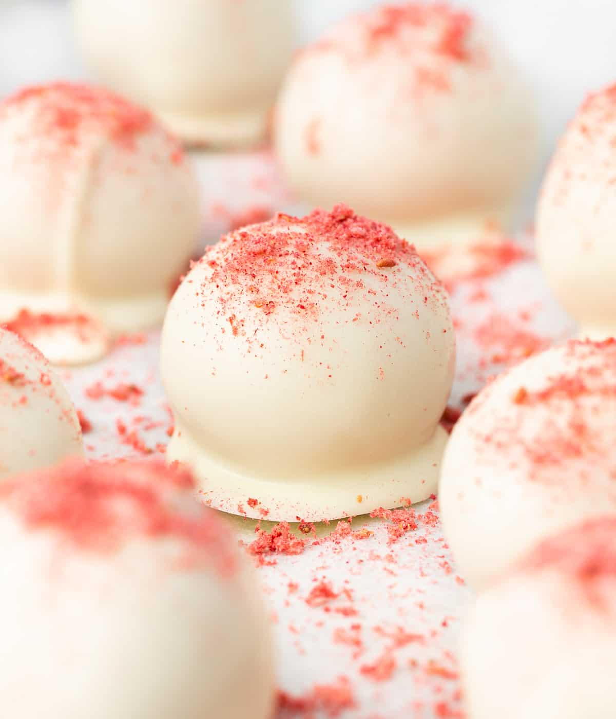 Dipped truffles sprinkled with strawberry powder on a lined baking tray.