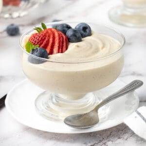 Vanilla mousse in a glass dessert cup placed over a small white plate and topped with fresh berries.