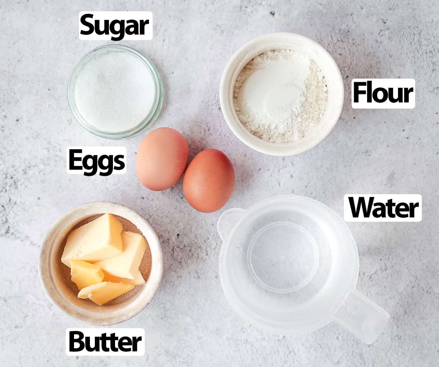 Ingredients for choux pastry on a light grey surface.