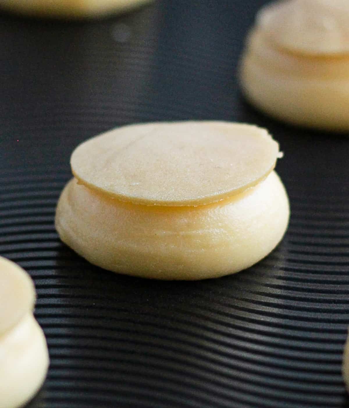 Disk of craquelin placed over a piped dollop of choux pastry on a baking tray.