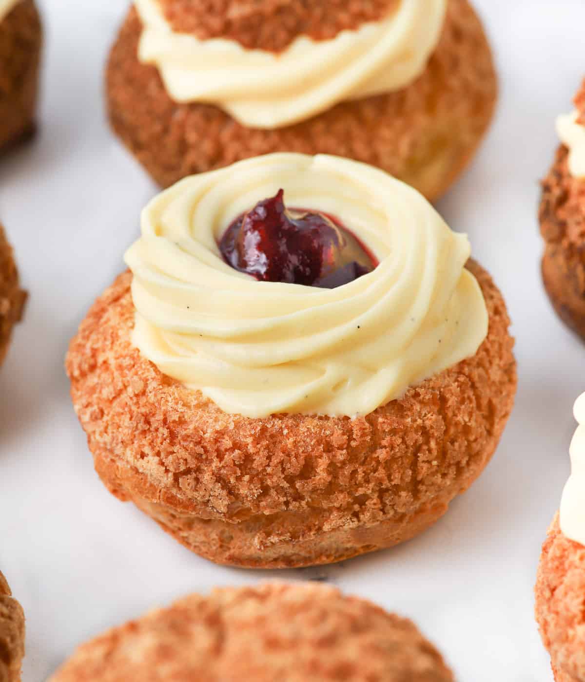 Vanilla custard piped over a choux sliced in half and filled with jam.