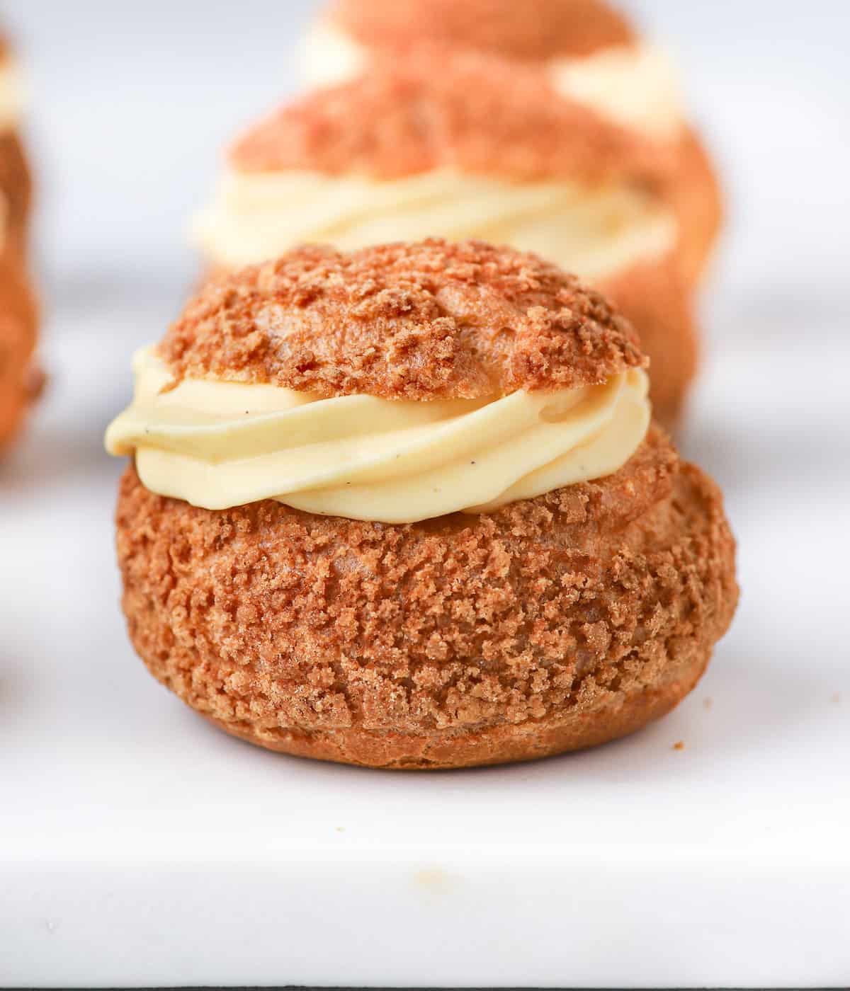 One choux filled with vanilla cream on a white surface.