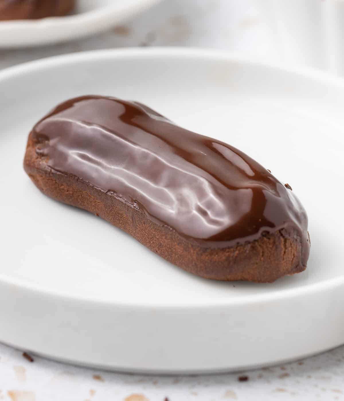 Close up on a glazed eclairs inside a small white shallow bowl.