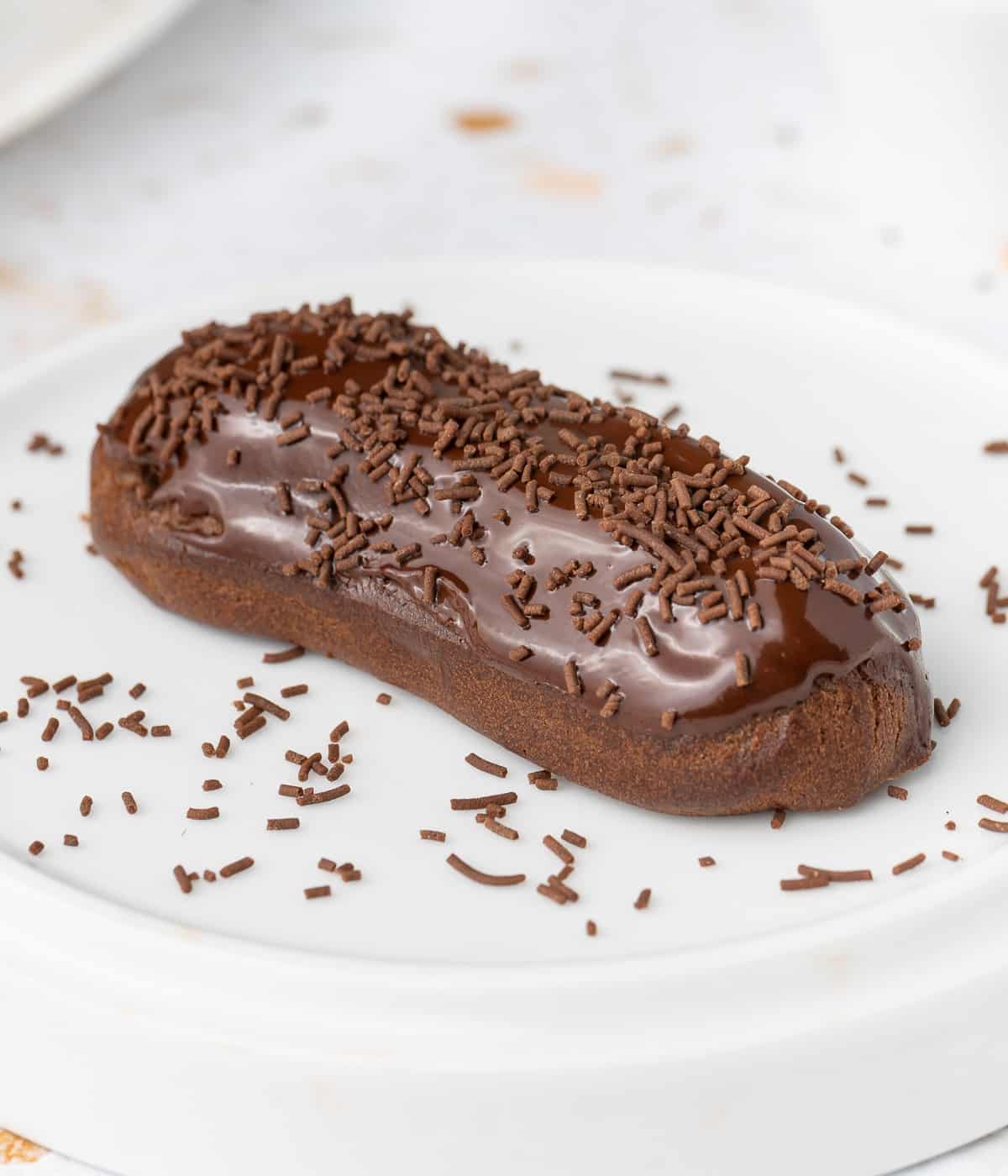 Eclair topped with chocolate sprinkles over a white plate.