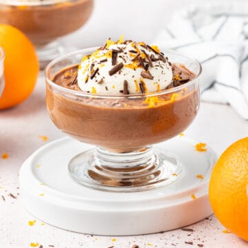 Mousse cup on a white plate surrounded by oranges.