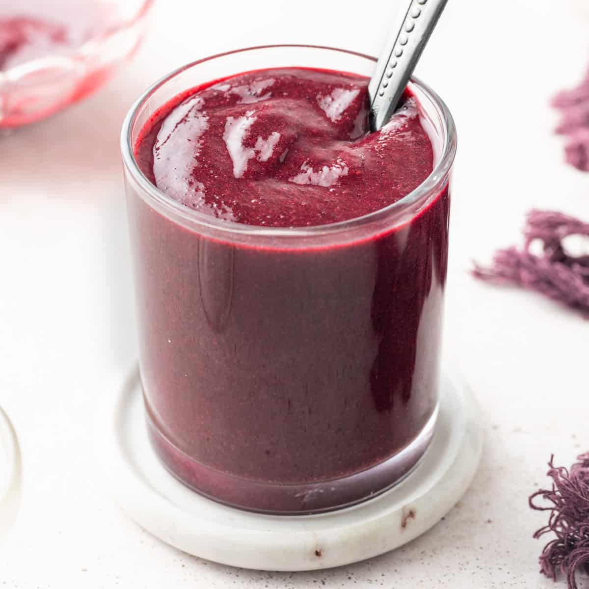 Glass full of berry coulis over a marble coaster with a silver spoon dipped in.