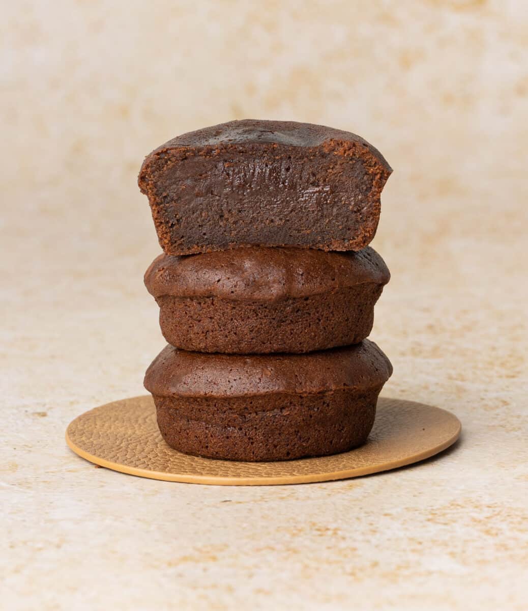 Stack of three chocolate cakes with the top one sliced in half.