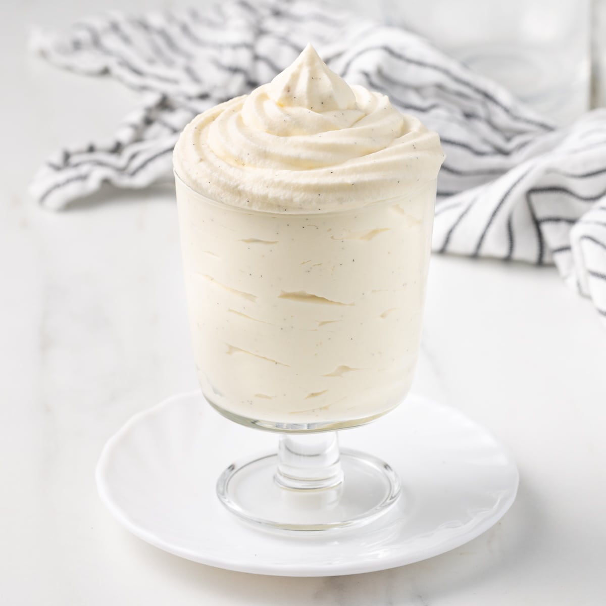 Cream piped inside a glass cup over a small white plate with a striped tea towel in the background.