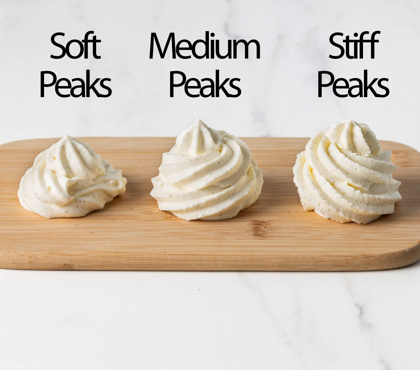 Dollops of chantilly cream at different whipping stages, piped over a small wooden board.