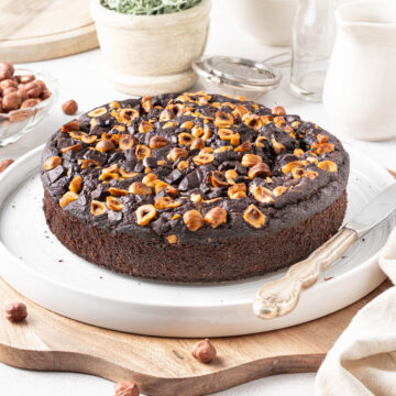 Cake on a large white plate placed over a wooden cutting board.