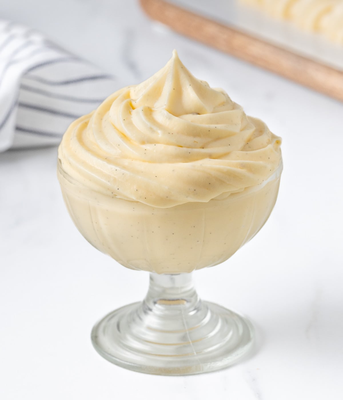 Cream piped into a small glass cup with a tea towel and serving board in the background.