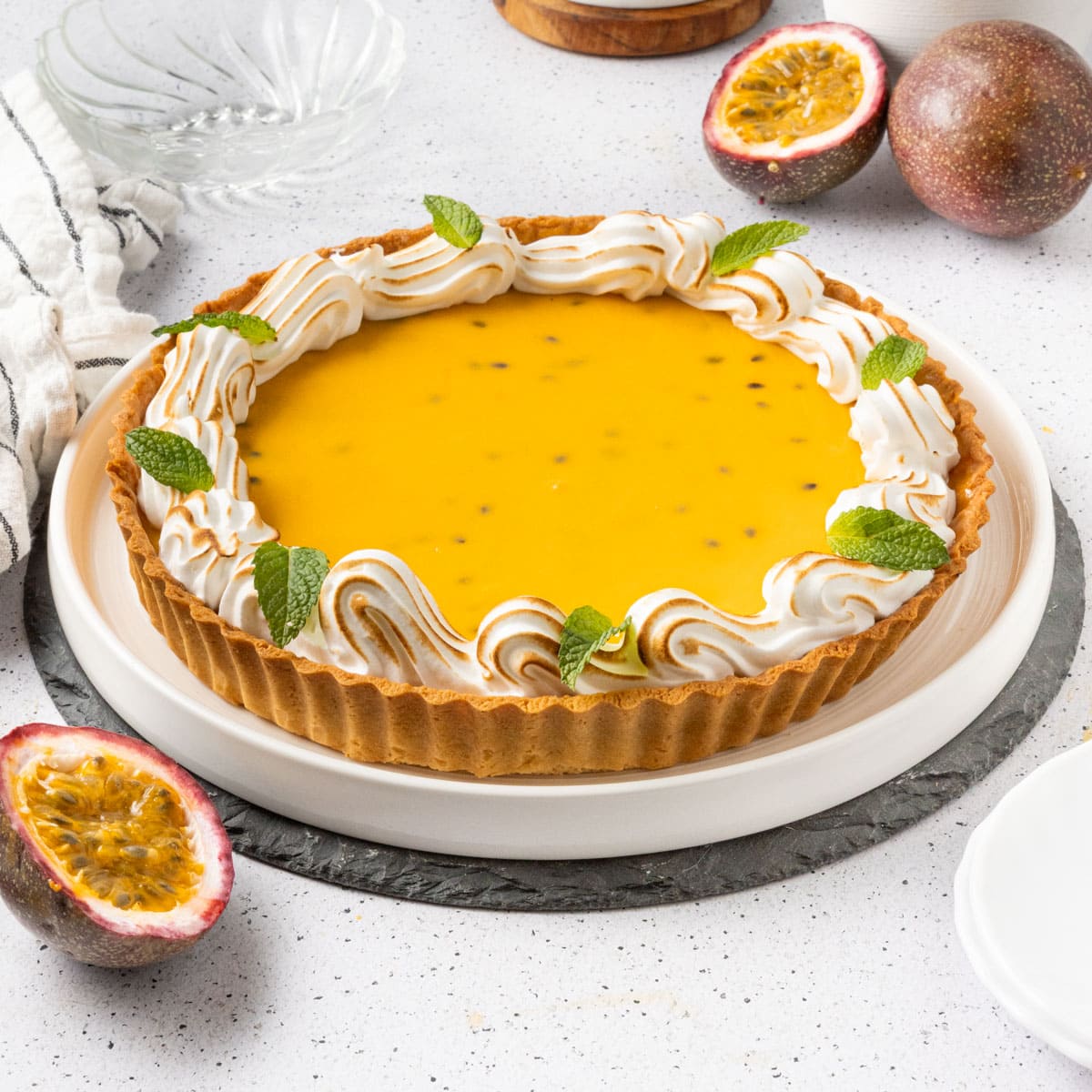 Passion fruit tart on a large white plate surrounded by fresh passion fruits.