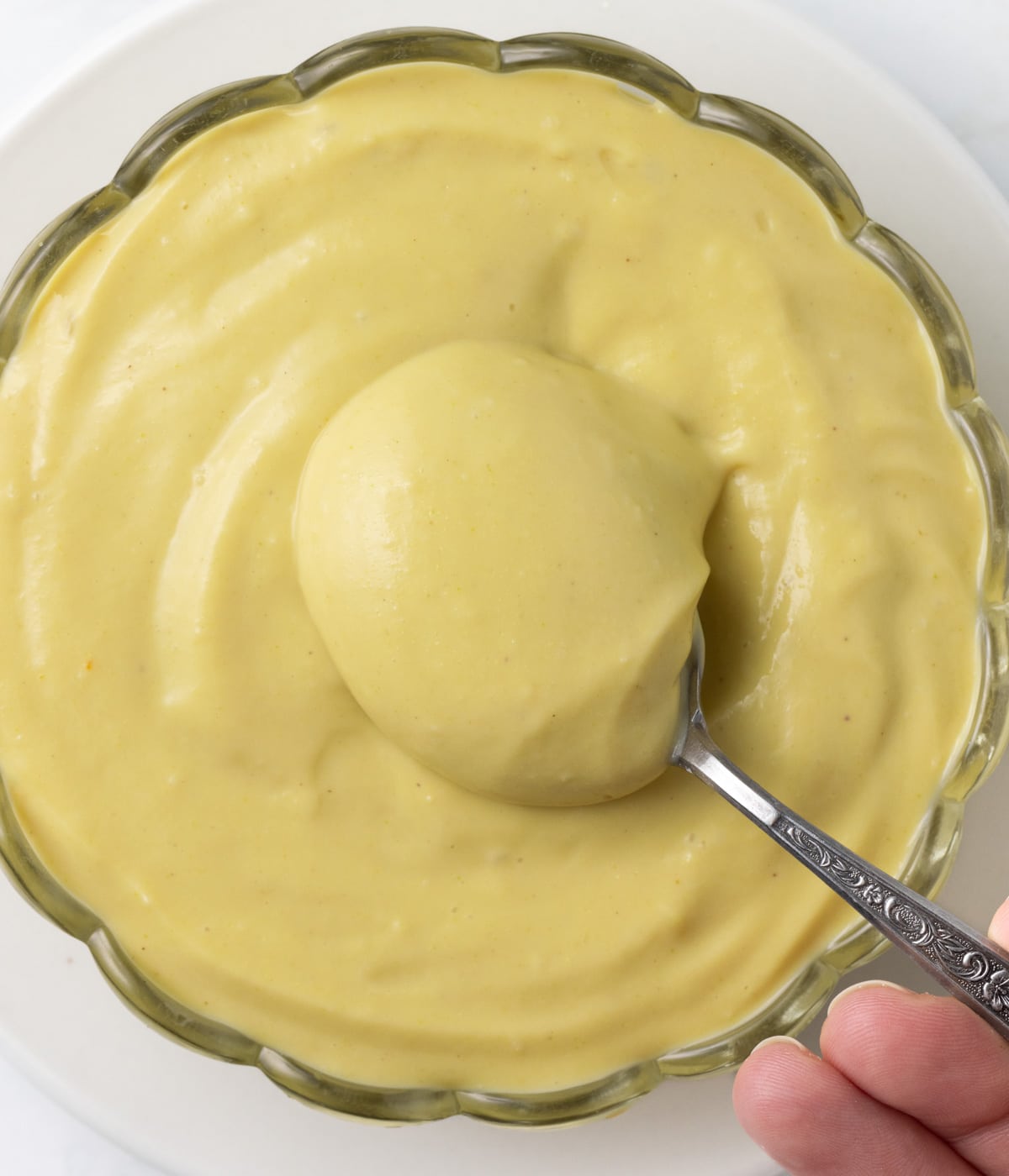 Picking up cream from a glass bowl with a spoon seen from above.