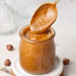 Silver spoon dipped in a small glass jar filled with hazelnut butter.