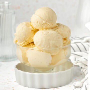 Ice Cream in a dessert cup inside a small white dish with striped napkin in the background.
