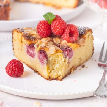 Front view of a slice of cake topped with fresh raspberries, with a bite taken off.