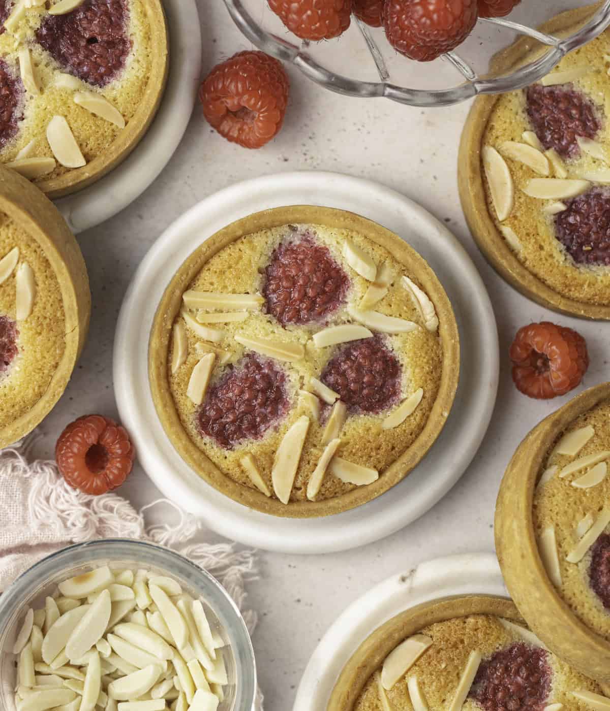 Tartlets and bowls of raspberries and slivered almond seen from above.